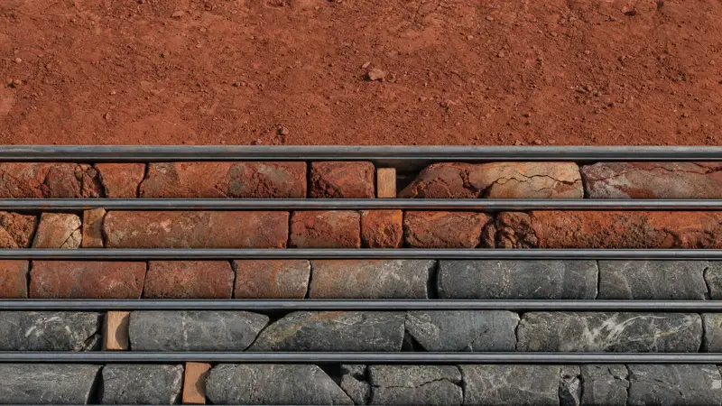 Rows of drill core in trays on red earth, grading from oxidised rock through to fresh